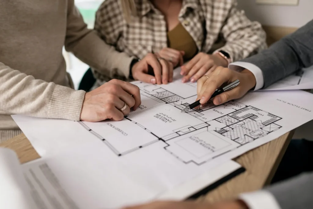 Gruppo di persone che esamina il progetto di una casa su planimetrie dettagliate, rappresentazione ideale di un servizio di consulenza finestre per la scelta delle soluzioni migliori.